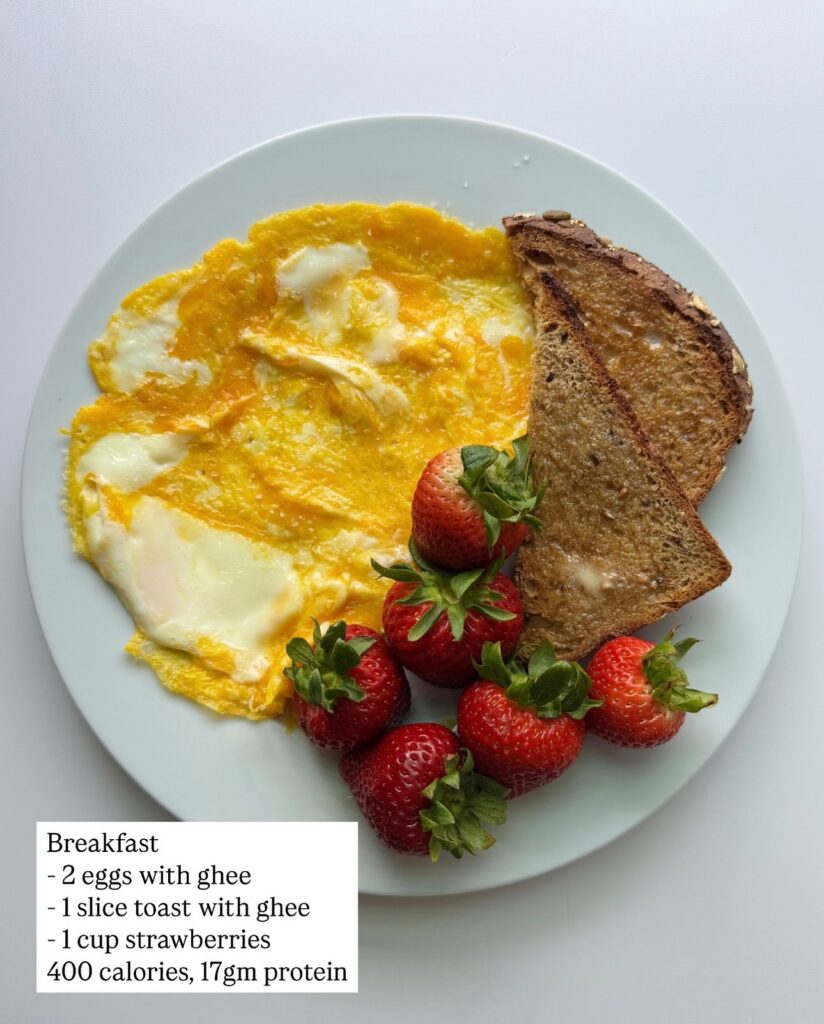 Two eggs cooked with ghee, whole grain toast with ghee, and strawberries with calorie and protein counts.