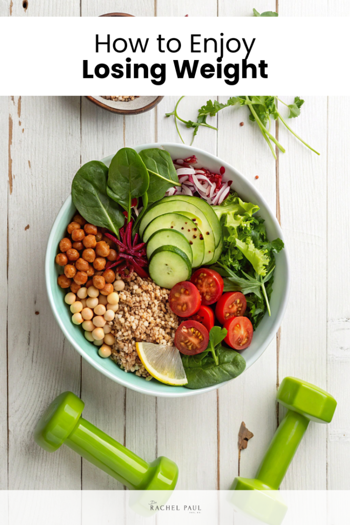 A colorful overhead shot of a healthy grain bowl filled with roasted chickpeas, cucumber slices, cherry tomatoes, spinach, red onion, quinoa, and a lemon wedge, styled on a white wood surface with green dumbbells beside it. Dr. Rachel Paul logo at the bottom.
