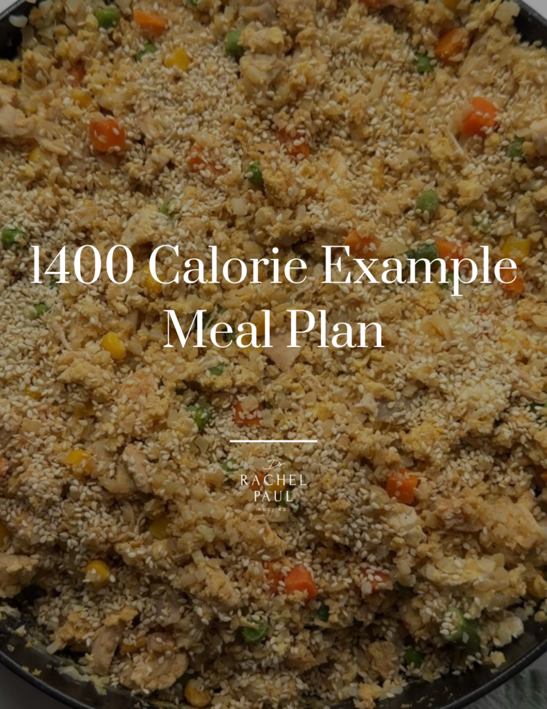 A close-up overhead view of a large pan filled with cauliflower rice, mixed with chopped carrots, peas, corn, and pieces of chicken, all topped with a generous amount of sesame seeds.