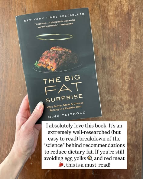 A hand holding "The Big Fat Surprise: Why Butter, Meat and Cheese Belong in a Healthy Diet" by Nina Teicholz. The dark book cover features a roasted meat dish with a golden halo above it and a New York Times Bestseller banner at the top. A text overlay reads "I absolutely love this book. It's an extremely well-researched (but easy to read) breakdown of the science behind recommendations to reduce dietary fat. If you're still avoiding egg yolks and red meat, this is a must-read."